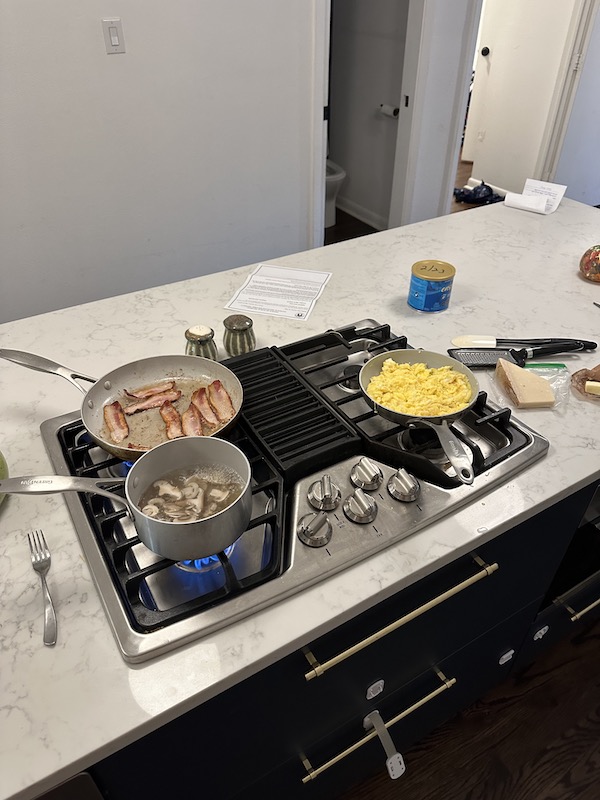 A stove, with a pan of small sizzling bacon strips